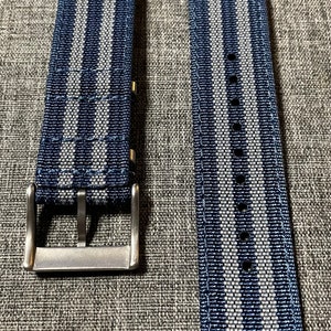May include: Two watch straps with a blue and white striped pattern. The straps are made of a woven fabric and have a silver buckle.