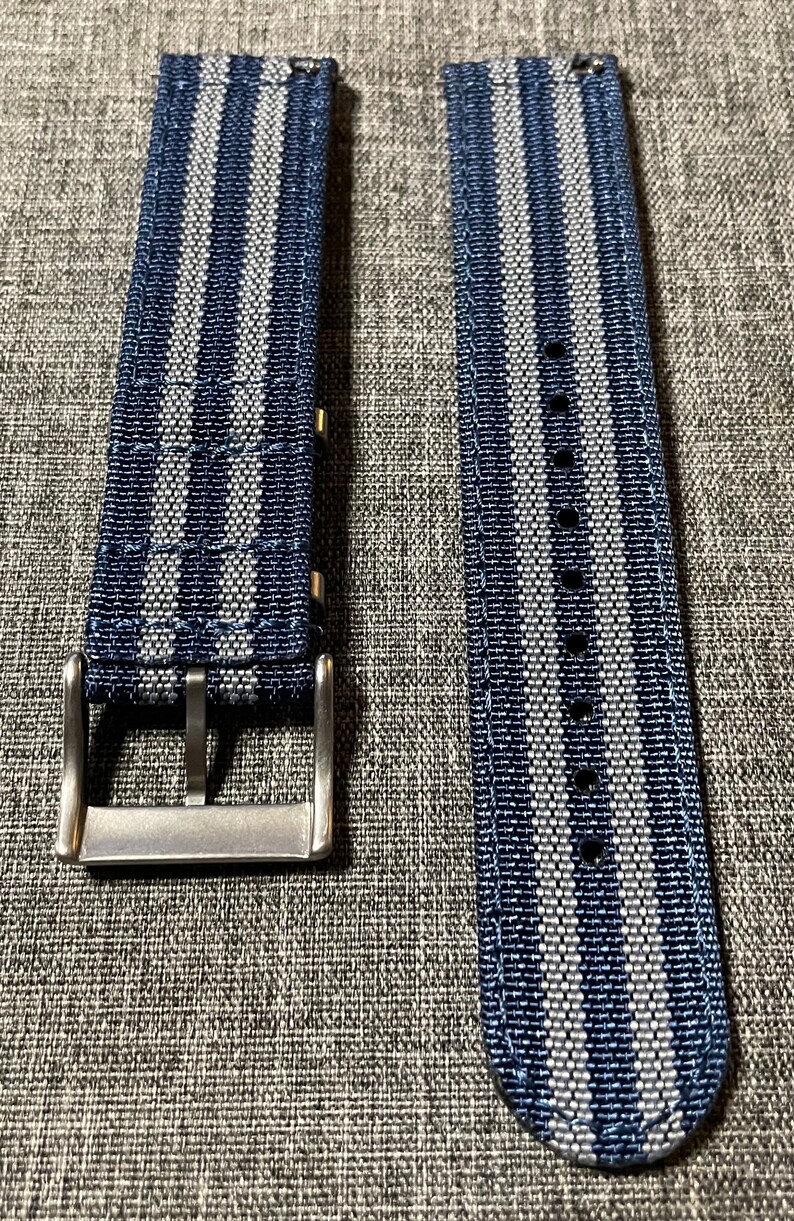 May include: Two watch straps with a blue and white striped pattern. The straps are made of a woven fabric and have a silver buckle.