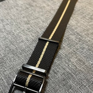 May include: A black watch strap with a white stripe down the center. The strap has a black metal buckle.