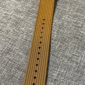 K&ouml;nnte beinhalten: Ein braunes Nylon-Armband mit silberner Hardware.
