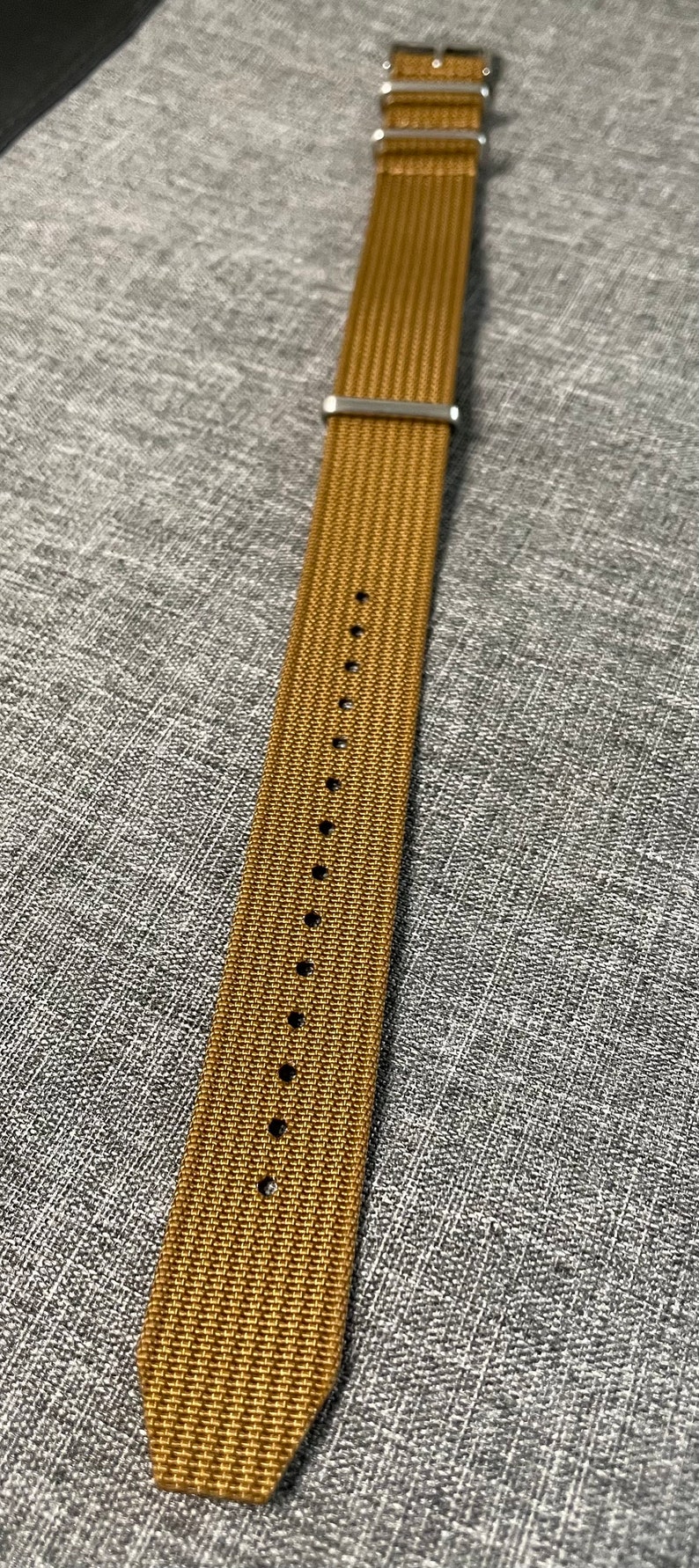 K&ouml;nnte beinhalten: Ein braunes Nylon-Armband mit silberner Hardware.