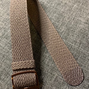 May include: A brown woven watch strap with a bronze buckle.