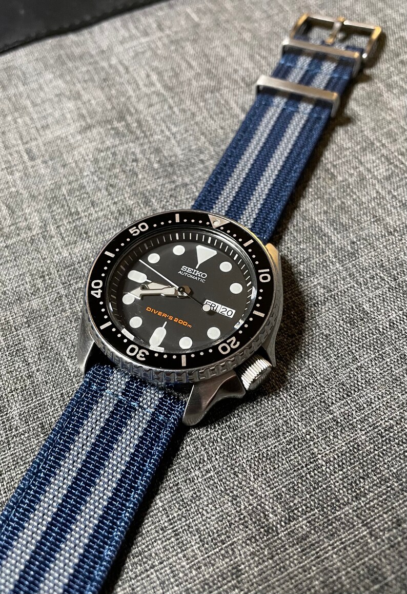 May include: A black Seiko automatic diver's watch with a blue and white striped nylon watch strap. The watch face has a black background with white markings and a date window that reads "FRI 20".