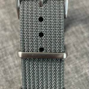May include: A gray nylon watch strap with a silver buckle and three keeper loops.