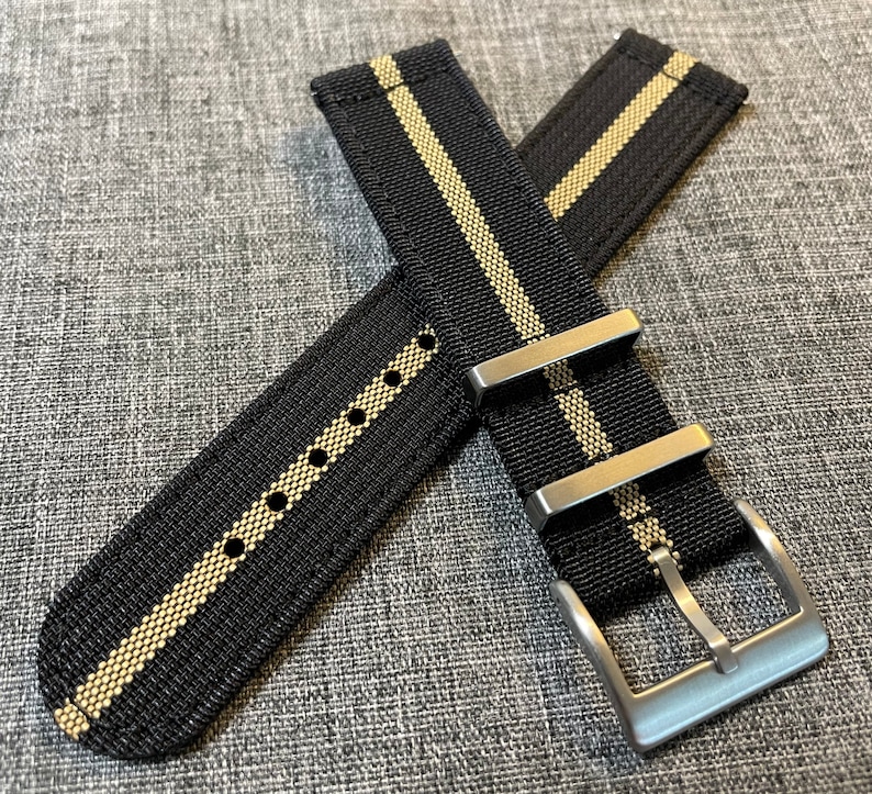 May include: Black watch strap with two white stripes and a silver buckle.