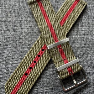May include: A green and red striped watch strap with a silver buckle. The strap is made of nylon and has a textured surface.