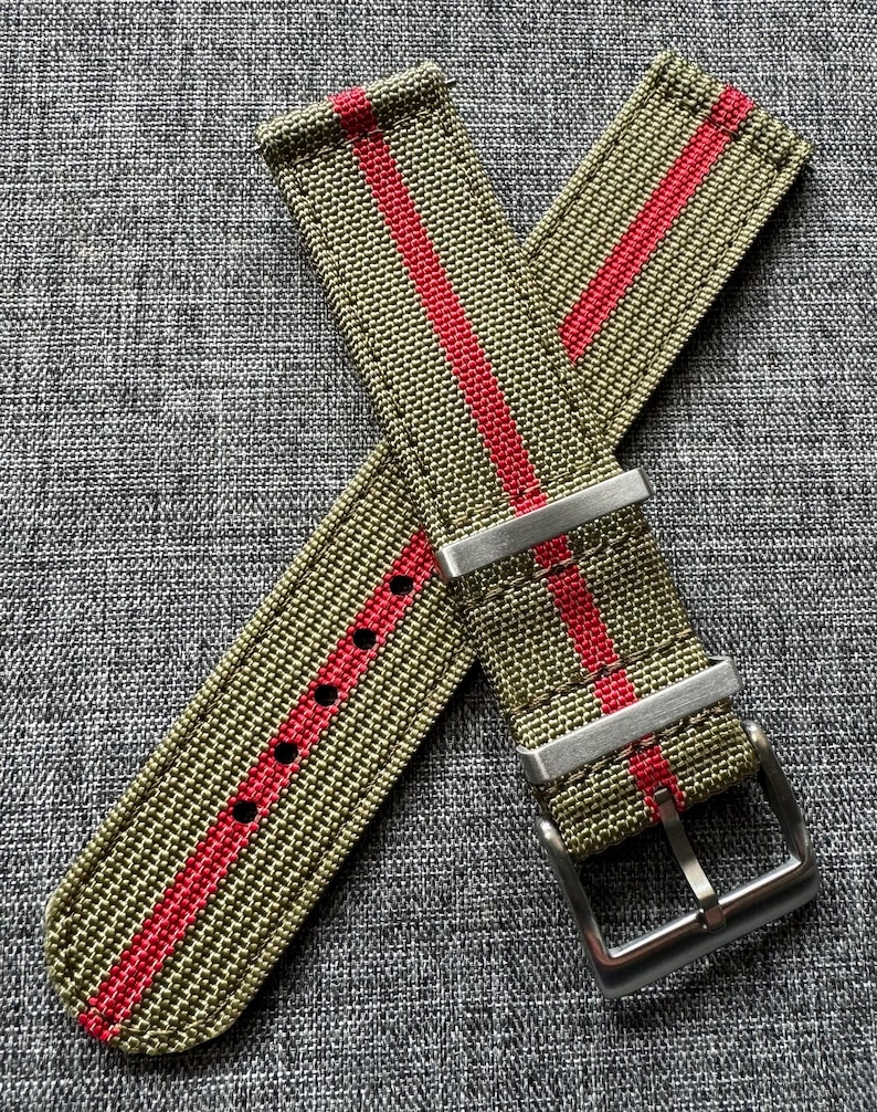 May include: A green and red striped watch strap with a silver buckle. The strap is made of nylon and has a textured surface.