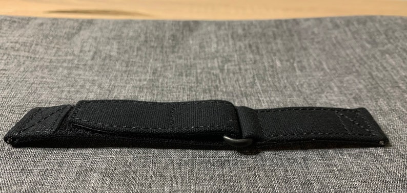 May include: Black watch strap with a buckle and stitching.