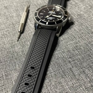 May include: A black watch with a black rubber strap. The watch face is black with white markings and a silver bezel. The watch has a date window at the 3 o'clock position.