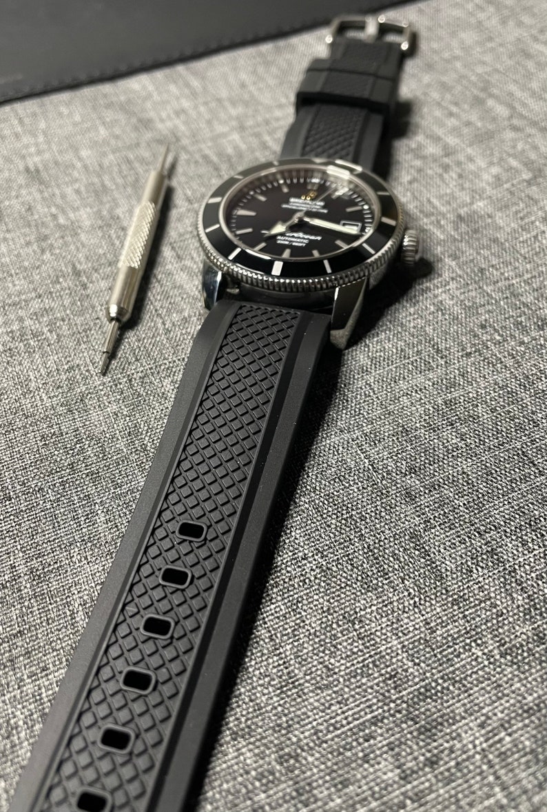 May include: A black watch with a black rubber strap. The watch face is black with white markings and a silver bezel. The watch has a date window at the 3 o'clock position.