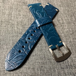 May include: A blue leather watch strap with a floral embossed pattern and a silver buckle.