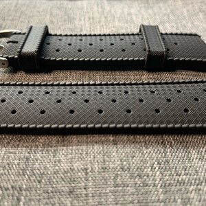 Puede incluir: Correa de reloj de caucho negro con un patr&oacute;n texturizado y agujeros para la ventilaci&oacute;n. La correa tiene una hebilla plateada.