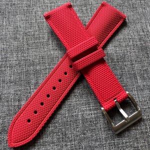 Puede incluir: Correa de reloj roja brillante con una superficie texturizada y una hebilla de acero inoxidable. La correa tiene m&uacute;ltiples orificios para ajuste y est&aacute; dise&ntilde;ada para sujetarse a una esfera de reloj. La correa est&aacute; hecha de un material duradero.