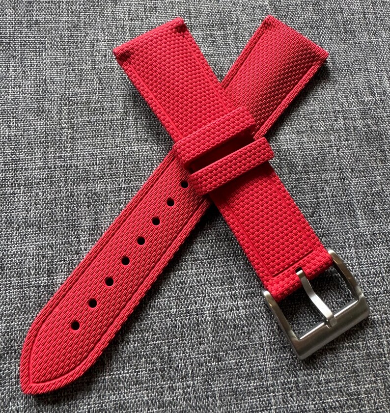 Puede incluir: Correa de reloj roja brillante con una superficie texturizada y una hebilla de acero inoxidable. La correa tiene m&uacute;ltiples orificios para ajuste y est&aacute; dise&ntilde;ada para sujetarse a una esfera de reloj. La correa est&aacute; hecha de un material duradero.