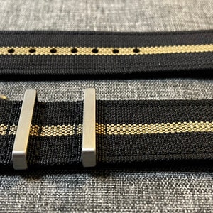 May include: A black watch strap with two thin beige stripes and a silver buckle.