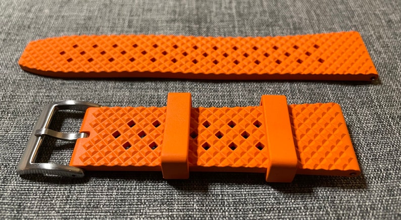 Puede incluir: Correa de reloj naranja con un patr&oacute;n de diamante texturizado y una hebilla plateada.