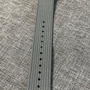 May include: A gray woven watch strap with silver hardware and multiple holes for adjusting the size.