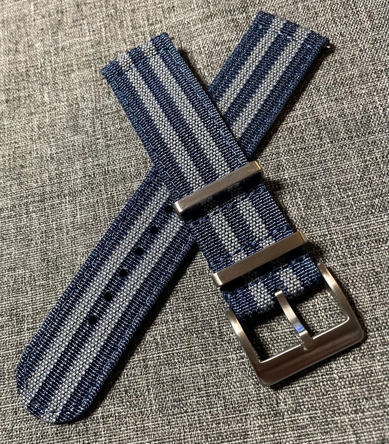 May include: A blue and gray striped watch strap with a silver buckle.