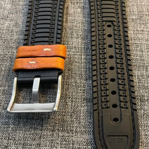 May include: A black and brown watch strap with a silver buckle. The strap has a textured design and the buckle has a smooth finish.