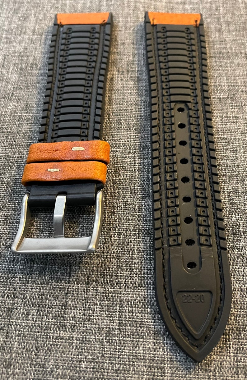 May include: A black and brown watch strap with a silver buckle. The strap has a textured design and the buckle has a smooth finish.