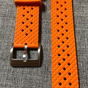 Puede incluir: Correa de reloj naranja con un patr&oacute;n de diamante texturizado y una hebilla plateada.
