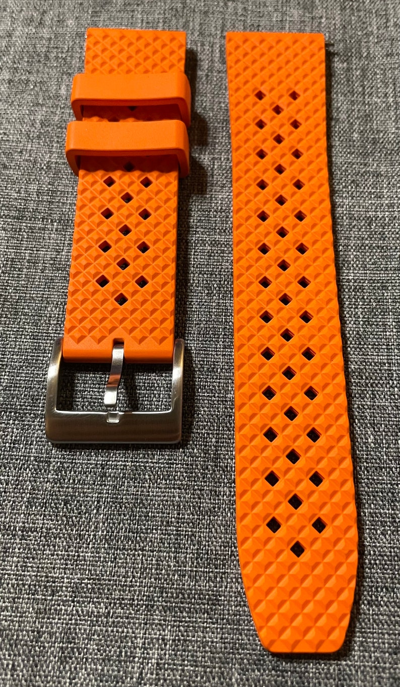 Puede incluir: Correa de reloj naranja con un patr&oacute;n de diamante texturizado y una hebilla plateada.