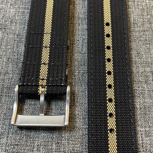 May include: Two black watch straps with a single gold stripe down the center. The straps have a silver buckle.