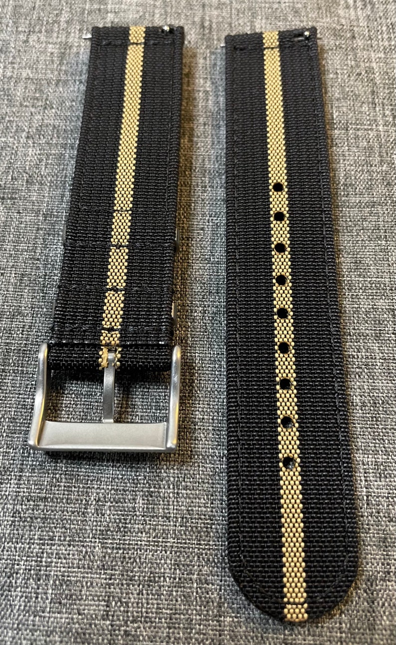 May include: Two black watch straps with a single gold stripe down the center. The straps have a silver buckle.