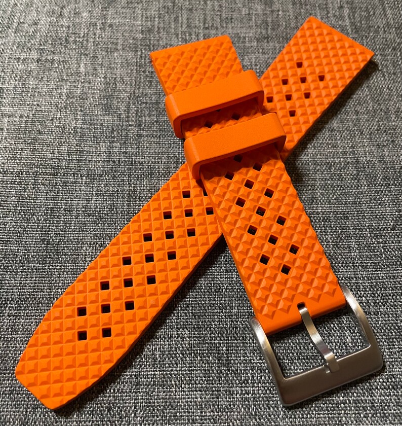 Puede incluir: Correa de reloj naranja con un patr&oacute;n de diamante y una hebilla plateada.