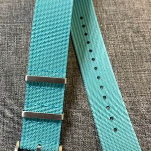 May include: A light blue nylon watch strap with silver buckle and keeper loops.