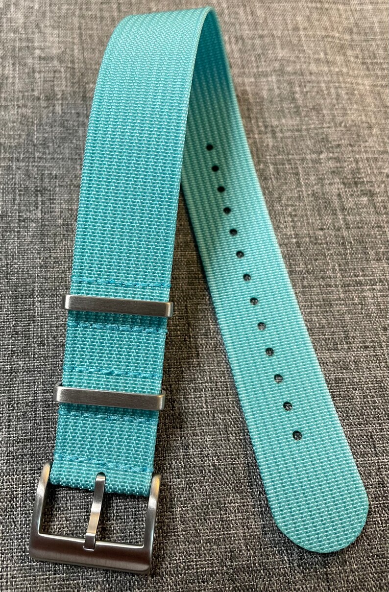 May include: A light blue nylon watch strap with silver buckle and keeper loops.