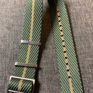 May include: A green and beige striped watch strap with a silver buckle. The strap is made of woven nylon and has a textured finish.