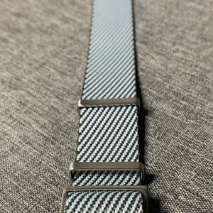 May include: A black and white striped watch strap with a silver buckle. The strap is made of a woven material and has a textured surface.