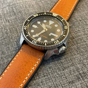 May include: A silver wristwatch with a black face and a brown leather strap. The watch face has white markings and the text "SEIKO AUTOMATIC" and "DIVER'S 200m".