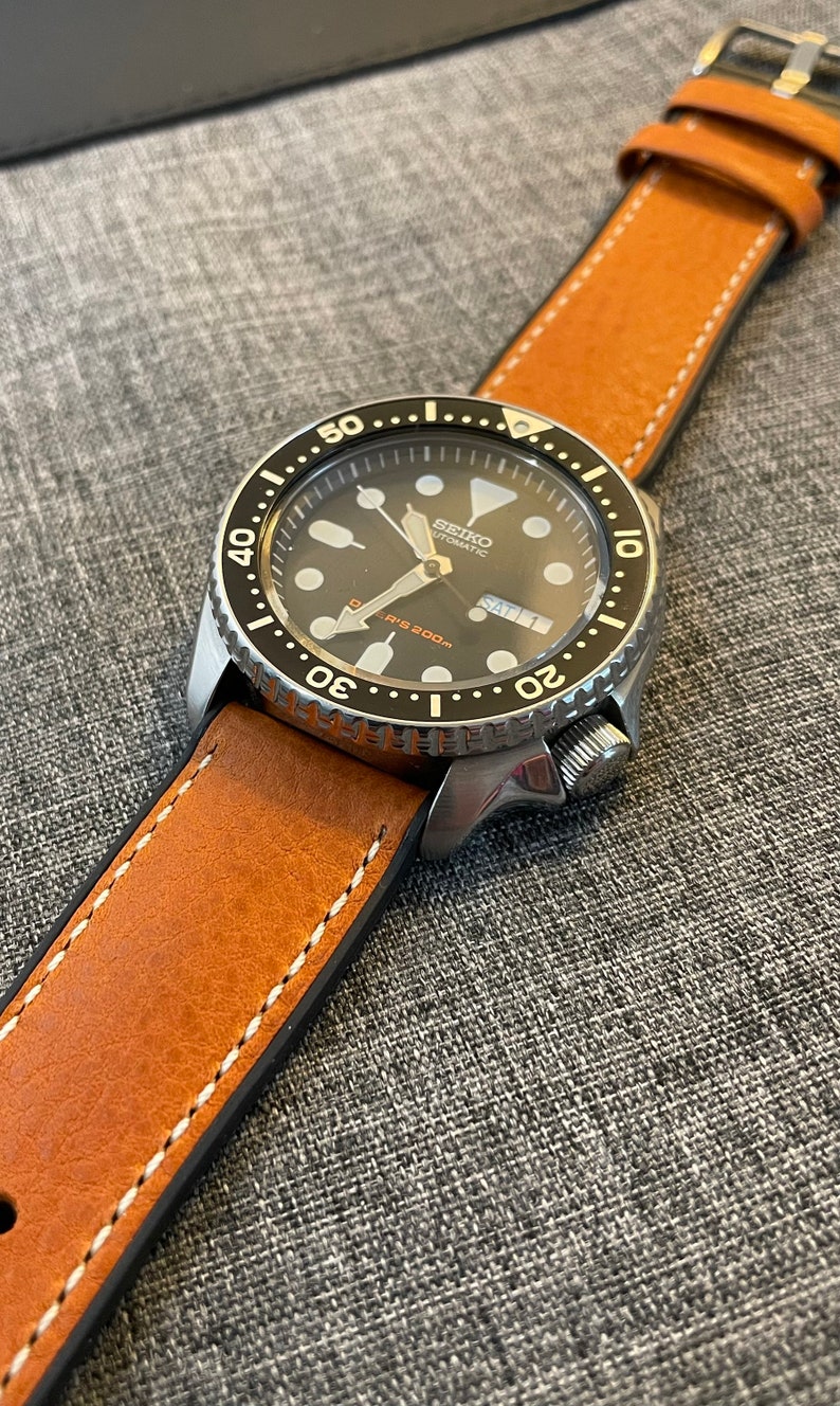 May include: A silver wristwatch with a black face and a brown leather strap. The watch face has white markings and the text "SEIKO AUTOMATIC" and "DIVER'S 200m".