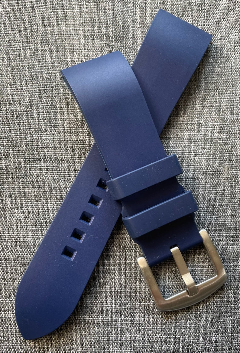 Puede incluir: Una correa de reloj azul marino con una hebilla plateada. La correa est&aacute; hecha de un material flexible y presenta cortes cuadrados cerca del extremo. La hebilla es rectangular con un acabado de metal cepillado.