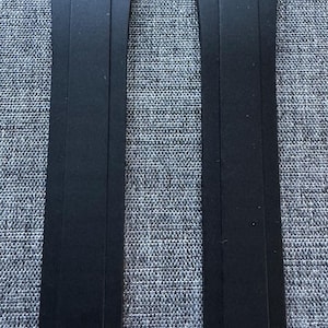 Puede incluir: Dos correas de reloj negras se muestran sobre un fondo gris texturizado. Cada correa es rectangular con un extremo curvo y un pasador de metal para la fijaci&oacute;n. Las correas est&aacute;n hechas de un material mate.