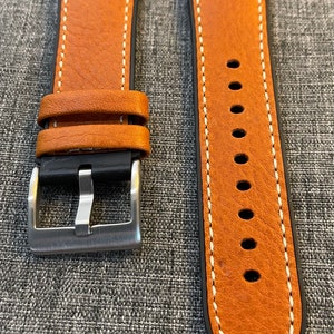 May include: Two brown leather watch straps with white stitching. The strap on the left has a silver buckle. The strap on the right has a pointed end.