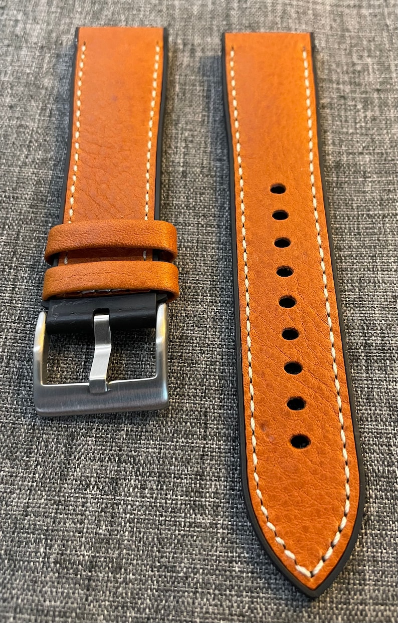 May include: Two brown leather watch straps with white stitching. The strap on the left has a silver buckle. The strap on the right has a pointed end.