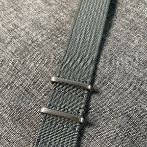 May include: A dark gray nylon watch strap with silver metal buckle and keepers.