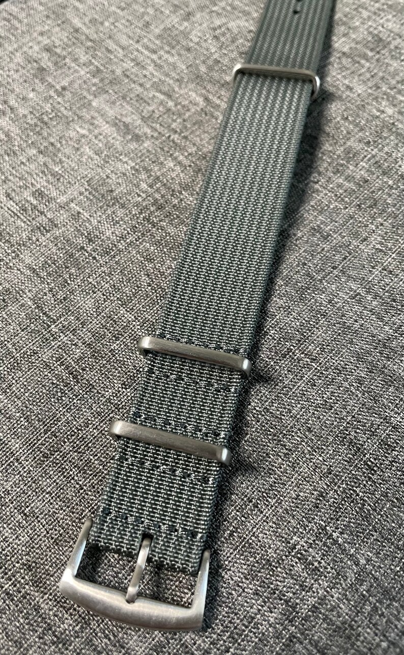 May include: A dark gray nylon watch strap with silver metal buckle and keepers.