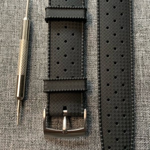 Puede incluir: Una correa de reloj de caucho negro con un patr&oacute;n texturizado y una hebilla plateada. La correa est&aacute; dise&ntilde;ada para un reloj con una anchura de leng&uuml;eta de 20 mm.