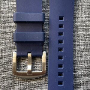 Puede incluir: Una correa de reloj azul marino con una hebilla de color plateado. La correa est&aacute; hecha de un material flexible y tiene una serie de agujeros cuadrados a lo largo de un lado. La hebilla es rectangular con una sola clavija.