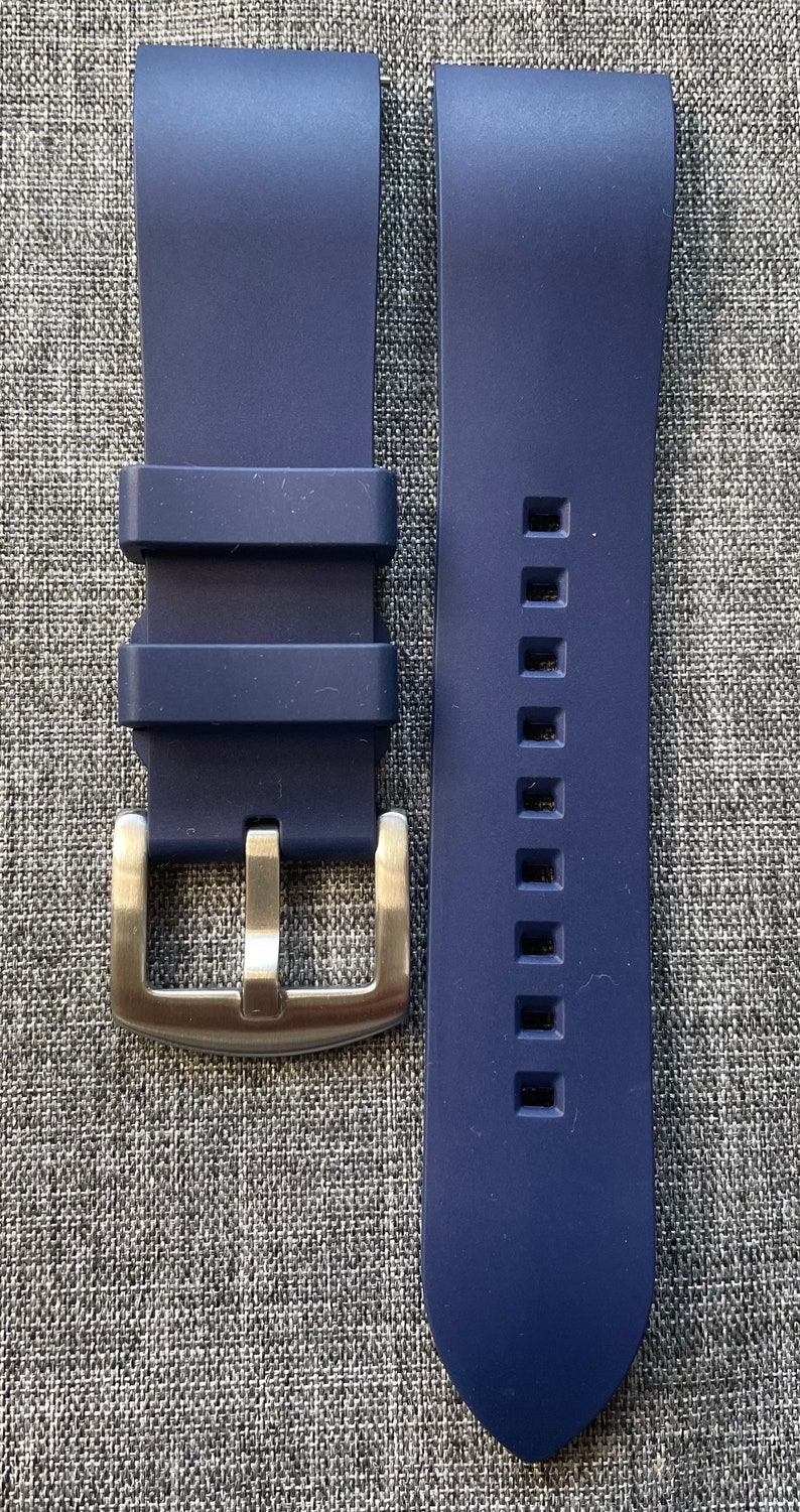 Puede incluir: Una correa de reloj azul marino con una hebilla de color plateado. La correa est&aacute; hecha de un material flexible y tiene una serie de agujeros cuadrados a lo largo de un lado. La hebilla es rectangular con una sola clavija.