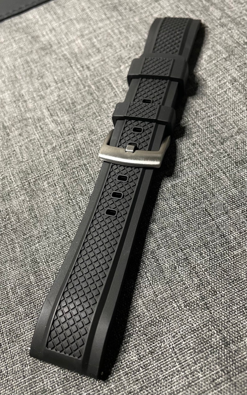 May include: Black rubber watch strap with a textured pattern and a silver buckle.