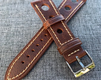 Könnte beinhalten: Braunes Lederarmband mit weißen Nähten und mehreren Löchern. Das Armband hat eine silberne Schließe.