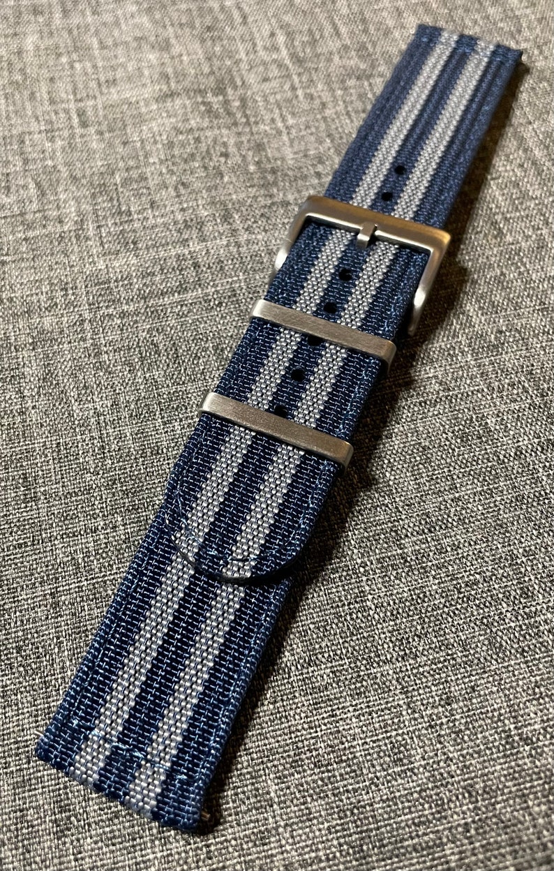 May include: A dark blue and silver striped watch strap with a silver buckle.