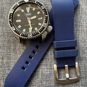 Puede incluir: Un reloj de buceo autom&aacute;tico Seiko con esfera negra, bisel de acero inoxidable y correa de caucho azul. La esfera del reloj tiene marcadores y agujas luminosas. La correa es de color azul oscuro y tiene una hebilla plateada.