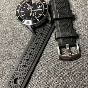 May include: A black Breitling Superocean watch with a black rubber strap. The watch has a silver bezel and a date window at the 3 o'clock position. The strap has a black rubber buckle.