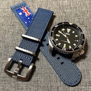 May include: A blue nylon watch strap with a silver buckle and a black and silver Seiko automatic watch with a black face and white markings. The watch has a rotating bezel with white numbers and markings.